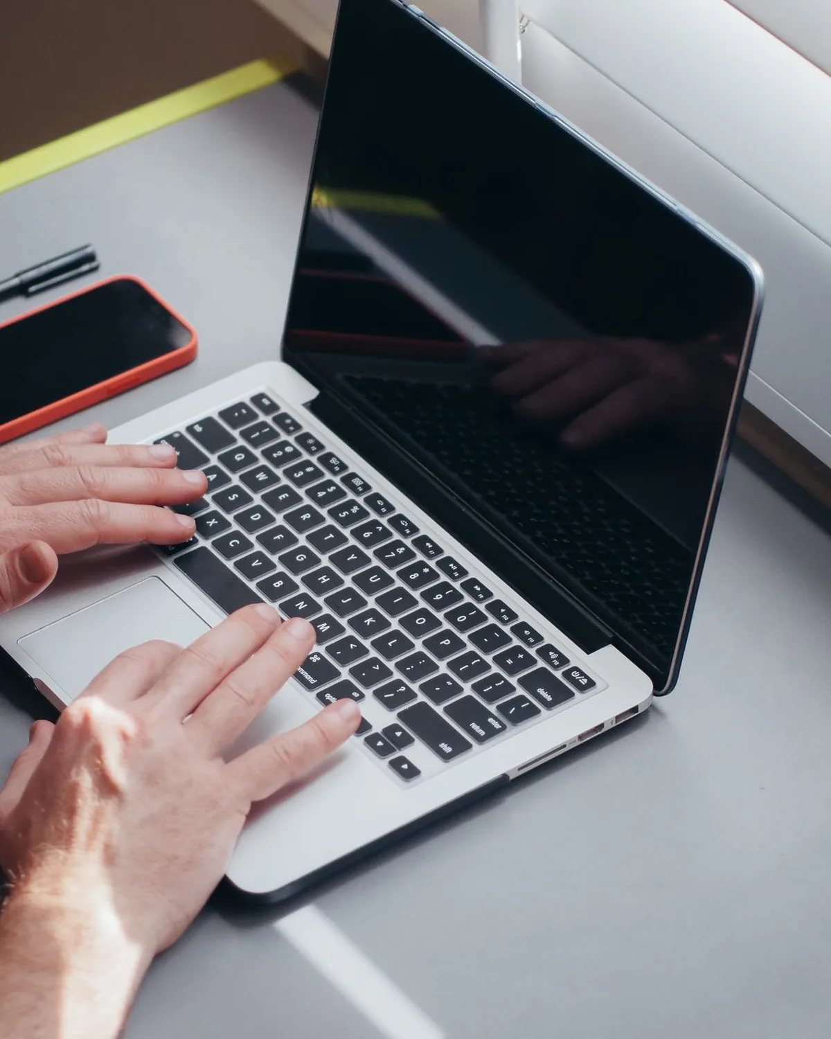 Hands working on a laptop with a phone on an office desk